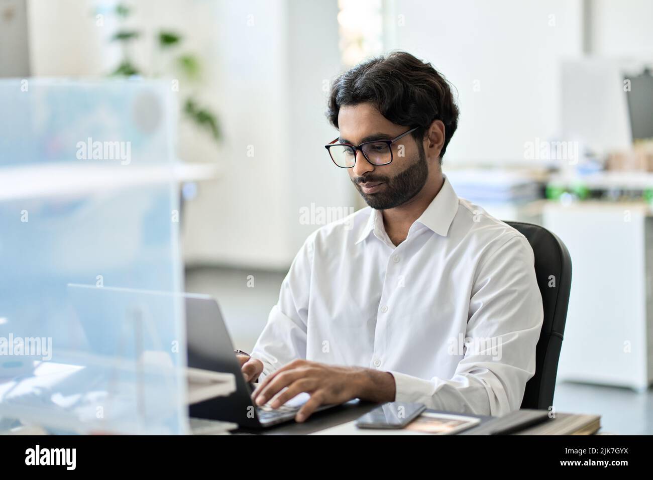 Giovane uomo d'affari indiano che lavora su un computer portatile seduto alla scrivania. Foto Stock