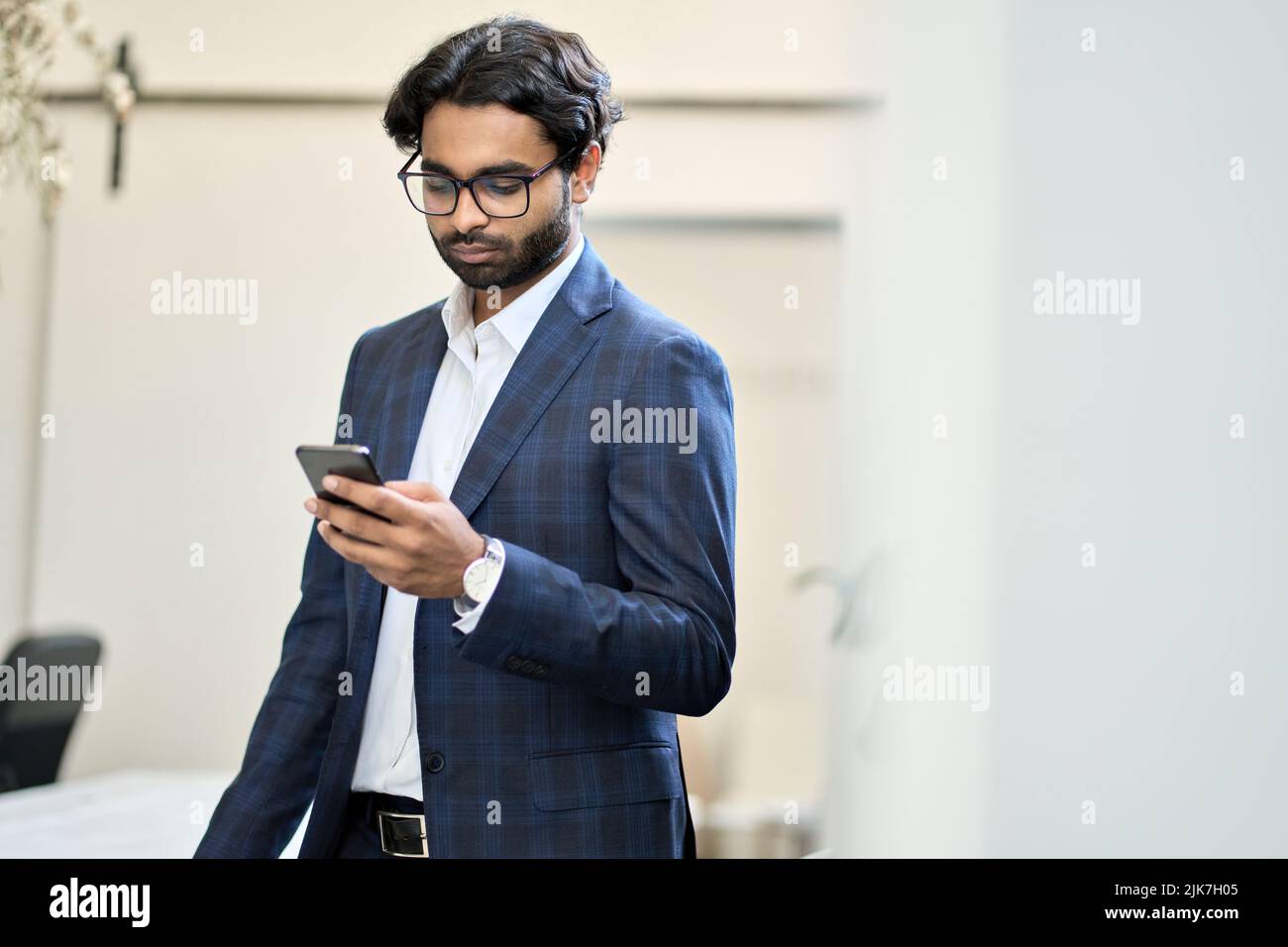 Un uomo d'affari indiano che utilizza uno smartphone che lavora in ufficio. Foto Stock