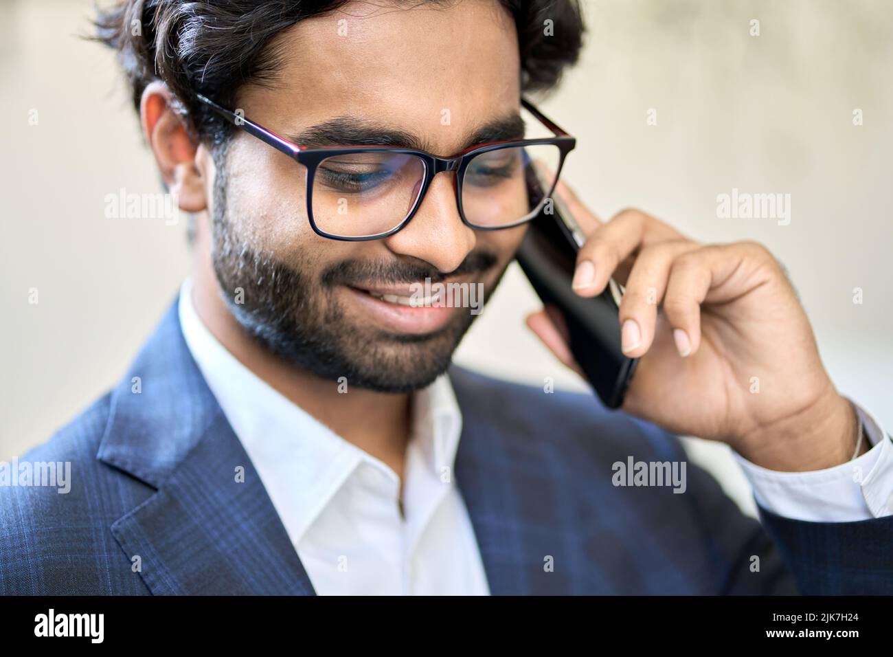 Uomo d'affari indiano sorridente che indossa il vestito che parla al telefono in ufficio. Foto Stock