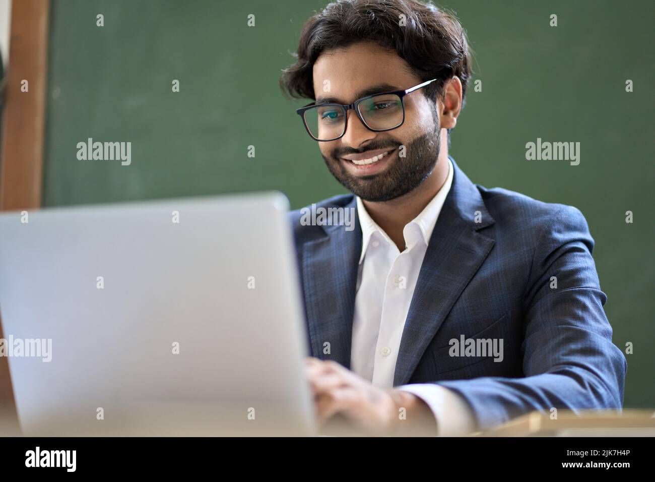 Sorridente uomo d'affari indiano con tuta da lavoro sul laptop. Foto Stock