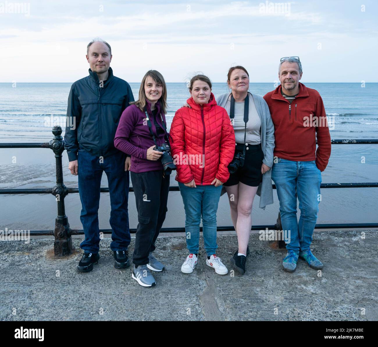 Gruppo familiare di cinque persone che si trovano insieme sul lungomare con vista sull'oceano Foto Stock