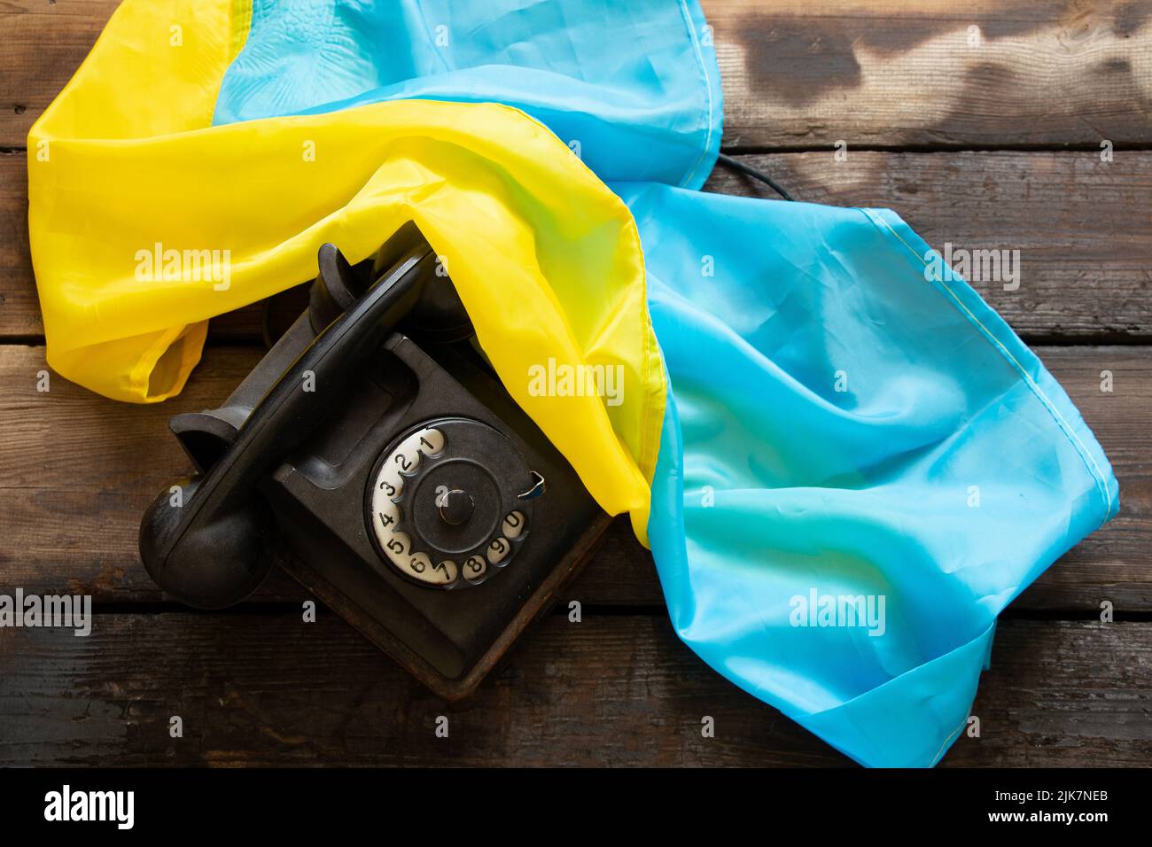 Un vecchio telefono nero e la bandiera dell'Ucraina giacciono su un tavolo di legno, il dialogo e la comunicazione Foto Stock