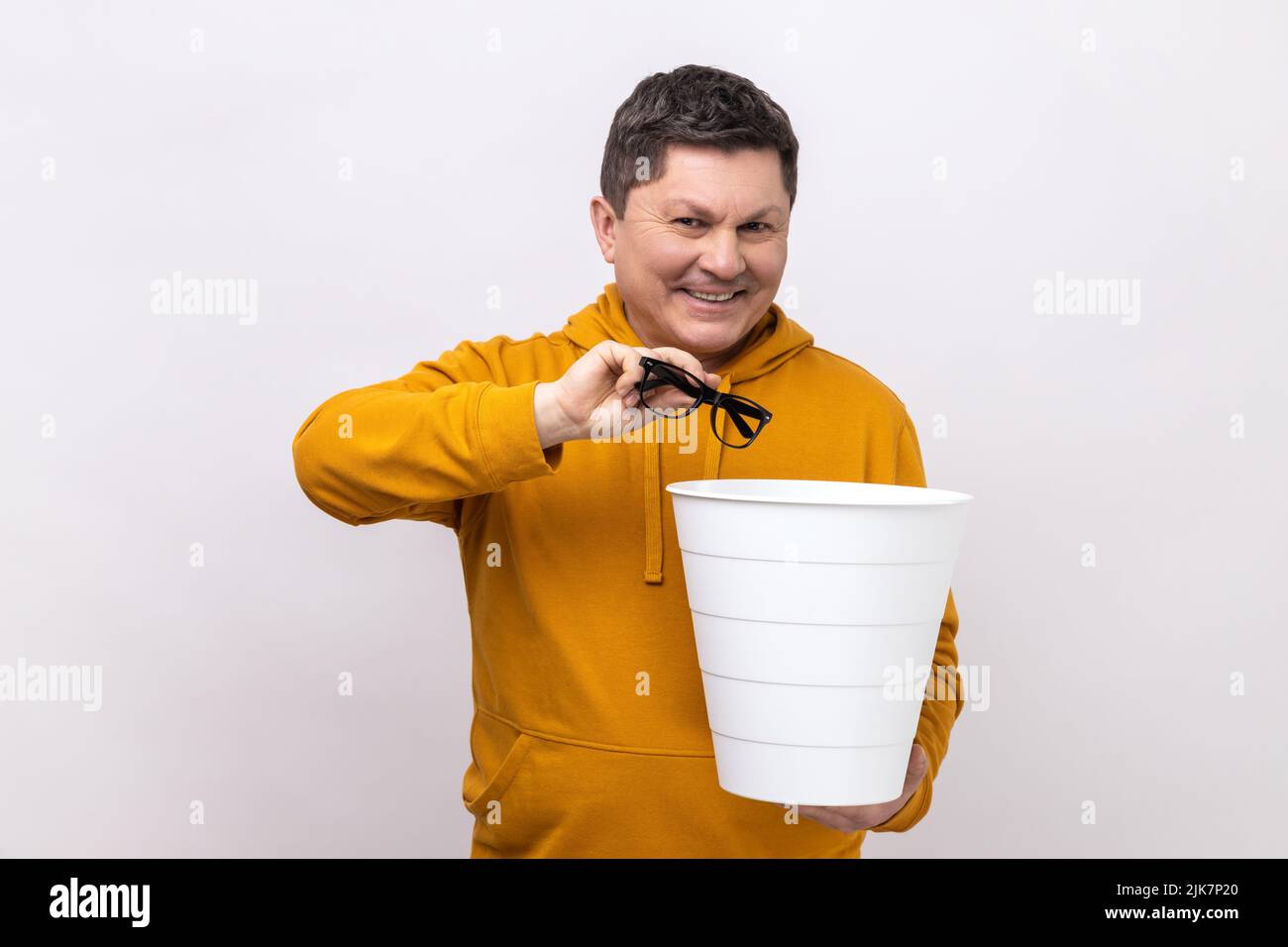 Ritratto di felice uomo di mezza età soddisfatto gettando fuori i suoi occhiali ottici dopo il trattamento di visione, guardando la macchina fotografica, indossando la felpa con cappuccio urban style. Studio interno girato isolato su sfondo bianco. Foto Stock