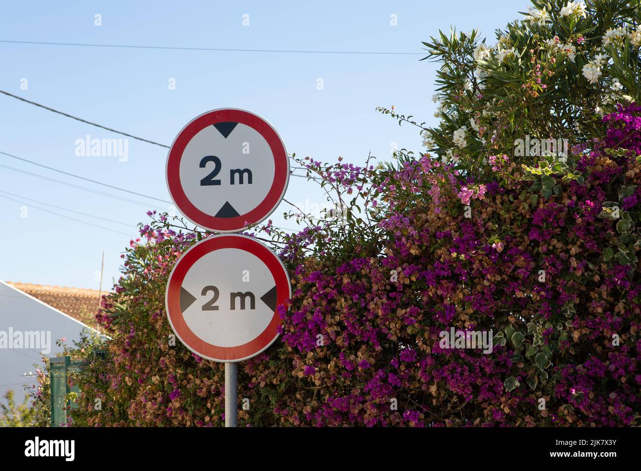 Raposeira, Portogallo. 20th luglio 2022. Su un muro, al di sopra del quale si arrampicano tre fiori, si trovano le indicazioni stradali che indicano il divieto di passaggio dei veicoli per la larghezza e l'altezza specificate di due metri. Credit: Viola Lopes/dpa/Alamy Live News Foto Stock