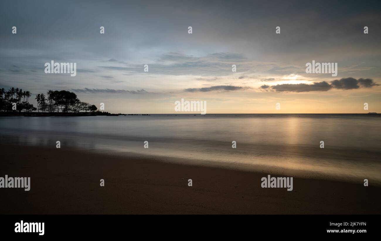 Lunga esposizione al tramonto sulla spiaggia tropicale con acque lisce e sfocate spiaggia di sabbia e alberi tropicali. Una bella spiaggia non sviluppata in Thailandia Foto Stock