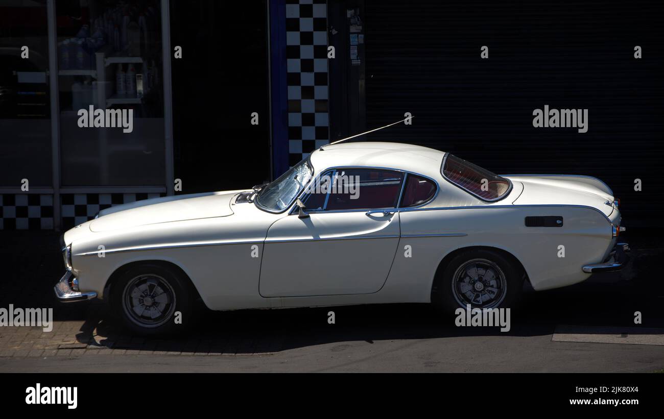 Un'auto Volvo P1800 S in bianco parcheggiata alla luce del sole e circondata dall'ombra Foto Stock