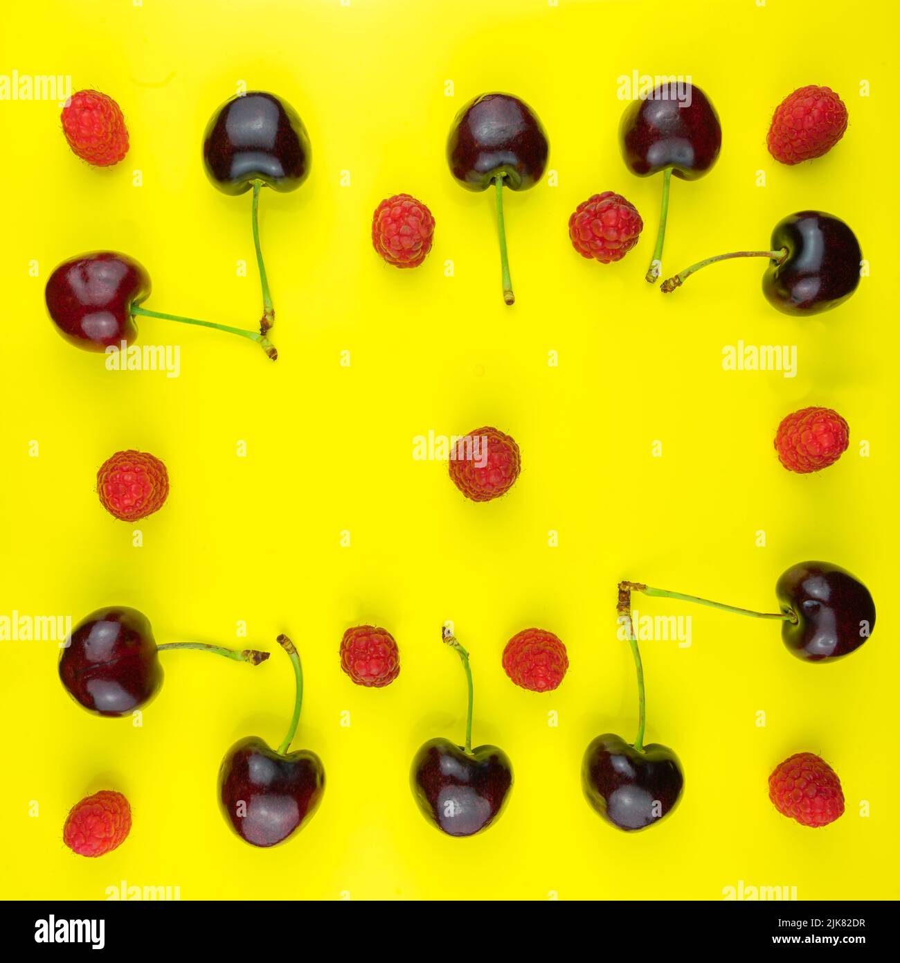 Linee di ciliegie rosse scure con gambi verdi e lamponi rossi e rosa su un campo giallo. Foto Stock