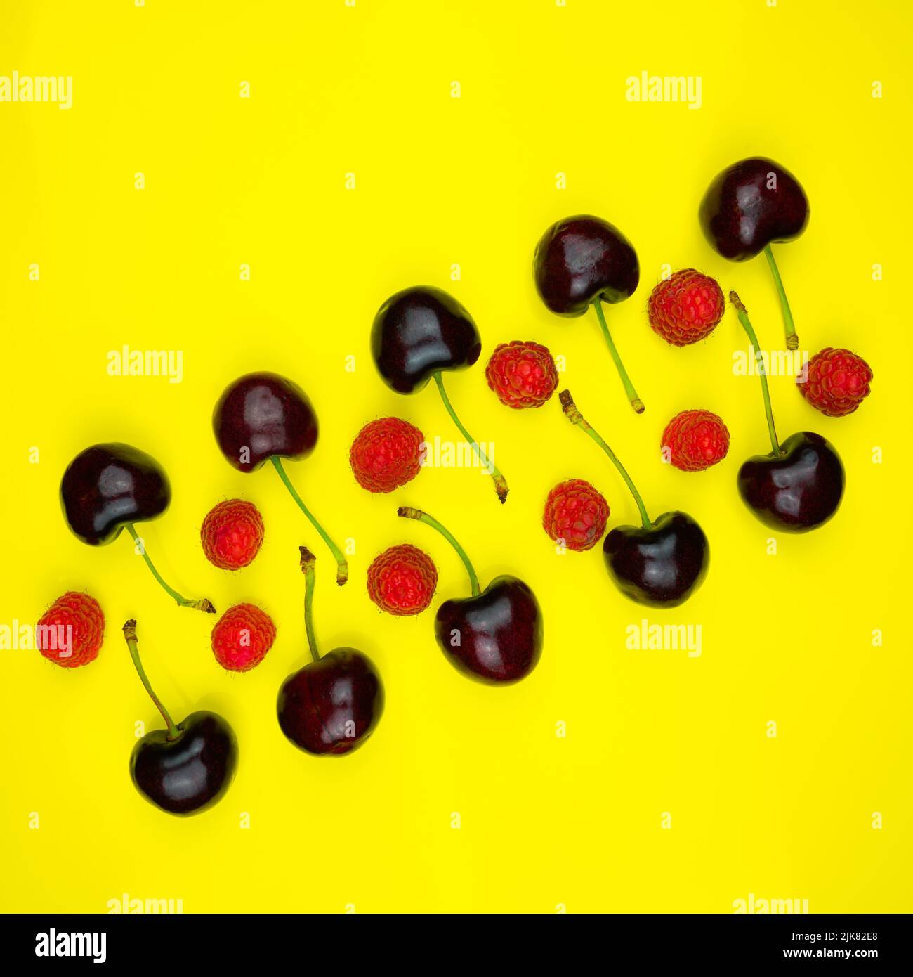 Linee di ciliegie rosse scure con gambi verdi e lamponi rossi e rosa su un campo giallo. Foto Stock