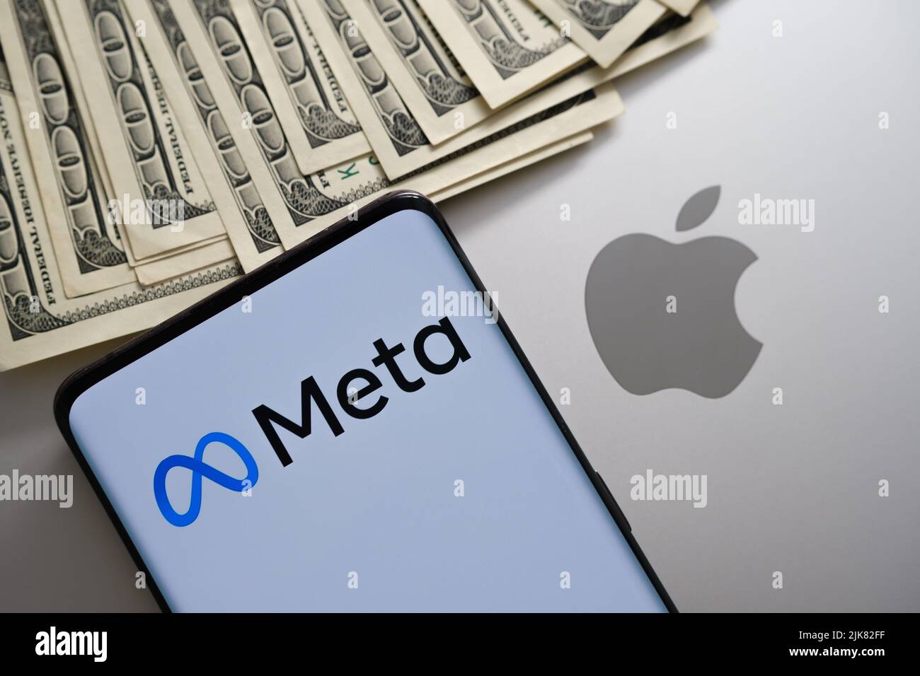 Logo aziendale meta visto su smartphone che viene messo in cima al macbook con logo di mela sfocata e dollari USA. Concetto. Stafford, Regno Unito, 20 luglio 2022 Foto Stock