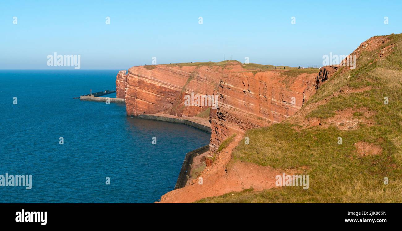 Alte scogliere rosse drammatiche dell'isola di Heligoland con in una bella giornata di sole. Giornata invernale a Helgoland nel Mare del Nord, Germania. Acque blu e rosse Foto Stock