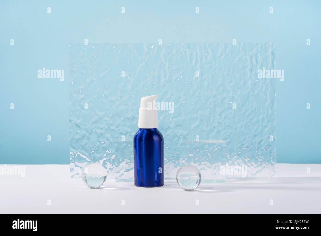 Boccale in crema metallizzata cosmetica su sfondo blu con eleganti puntini, sfere di vetro e piastra acrilica. Lozione bianco senza marchio prodotto di bellezza Foto Stock