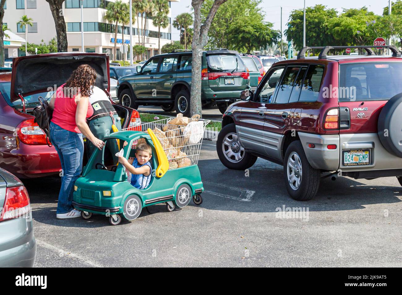 Miami Florida, shopping centro commerciale centro commerciale parcheggio auto parcheggio, donna ispanica madre afferrare ragazzo figlio carrello come veicolo backup prevenzione incidenti Foto Stock