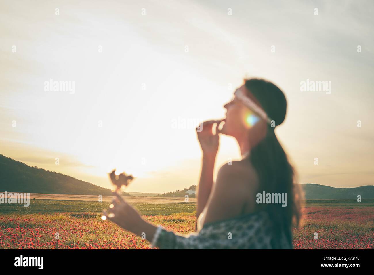 Una donna che mangia fragole al tramonto in un campo di papaveri. Messa a fuoco selettiva. Immagine sfocata. Vista frontale. Foto Stock
