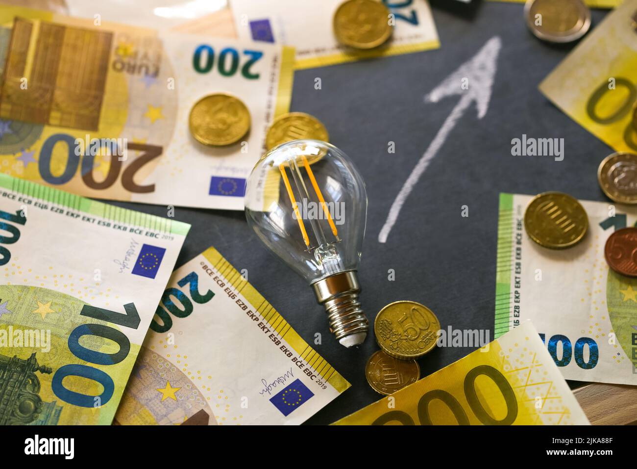 Elettricità cost.Rising i prezzi dell'elettricità in Europa. Lampadina, euro bollette e monete, su arrogato su una black board.Crisis di produzione di energia in Foto Stock
