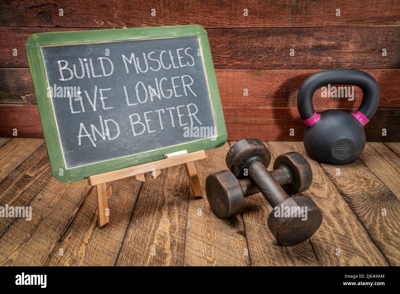 costruisci i muscoli, vivi più a lungo e meglio: testo ispirativo su una lavagna con manubri e kettlebell, fitness e concetto di longevità Foto Stock