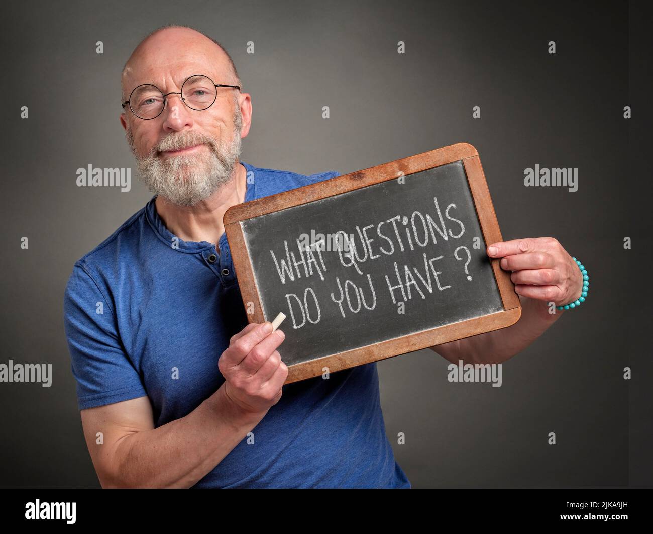 Quali domande avete? L'uomo anziano, l'insegnante, il presentatore o il mentore, sta tenendo una lavagna dell'ardesia con il testo bianco del gesso. Istruzione e comunicazione Foto Stock