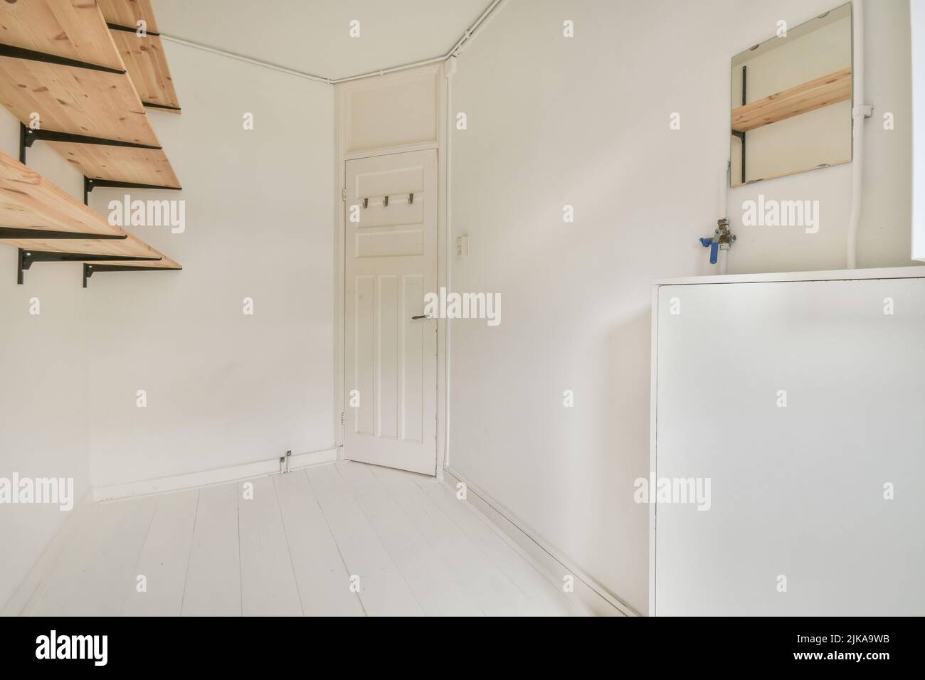 Interno di appartamento vuoto moderno con design geometrico con porta d'ingresso e pareti bianche e pavimento piastrellato illuminato con lampada Foto Stock