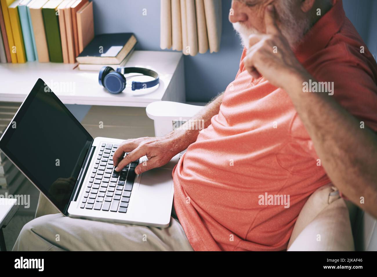 Uomo anziano che tiene il laptop in grembo e naviga in rete a casa Foto Stock