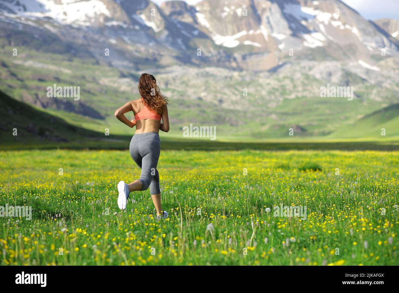 Indietro Visualizza il ritratto completo di una donna runner che corre in un campo in alta montagna Foto Stock