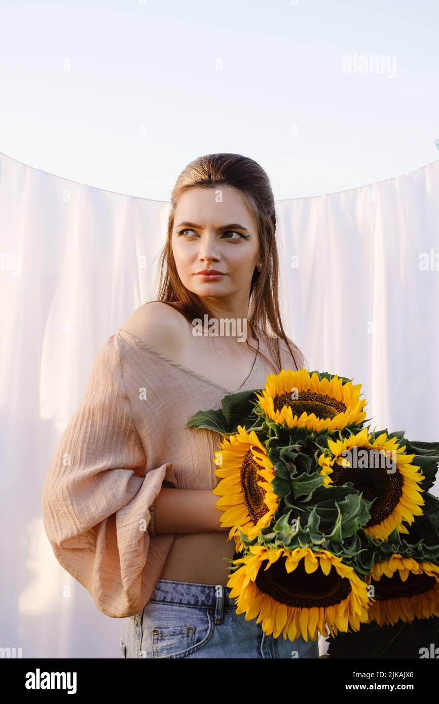 Donna romantica con girasoli su sfondo bianco tessuto all'aperto. Pelle pulita e bellezza naturale. Vacanze estive rurali Foto Stock