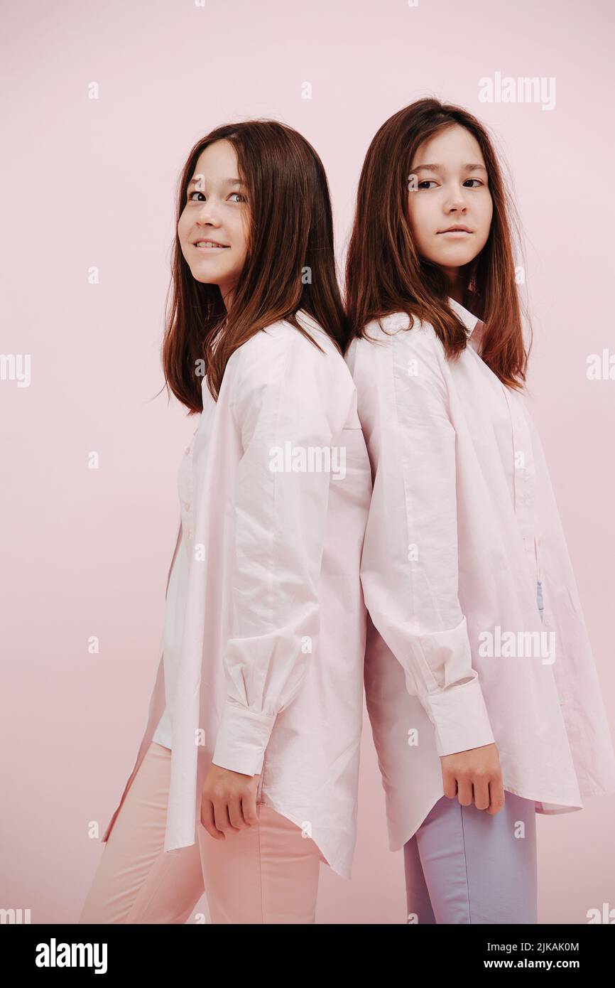 Adorabili ragazze gemelle graziose che si levano in piedi di nuovo alla parte posteriore, guardando sopra la spalla Foto Stock