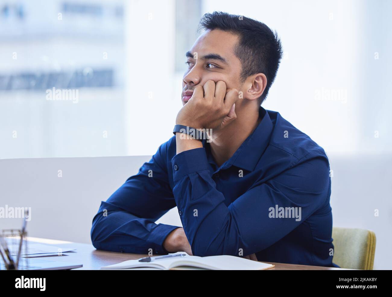 Non fare altro che sperare che tutto venga fatto... un giovane uomo d'affari che guarda annoiato mentre lavora in ufficio. Foto Stock