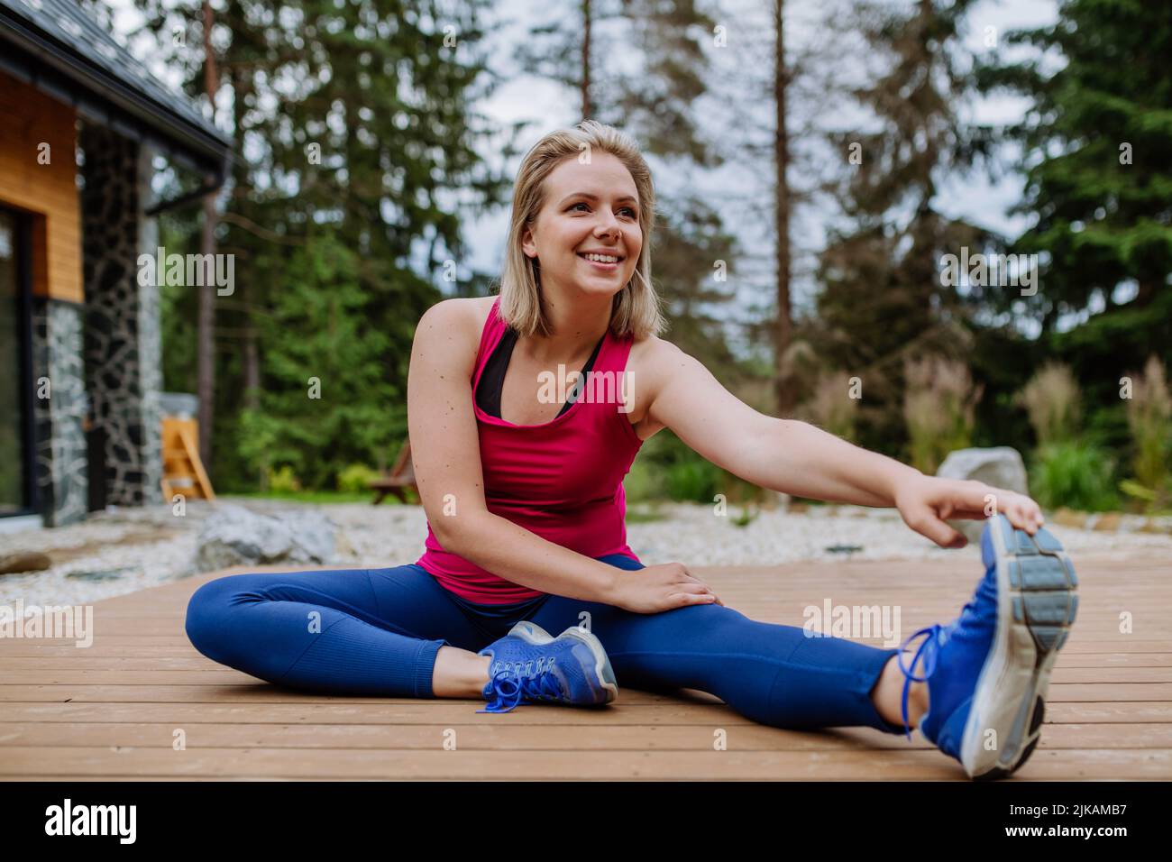 Giovane donna che pratica yoga, che si estende su un patio cottage di montagna circondato dalla natura. Foto Stock