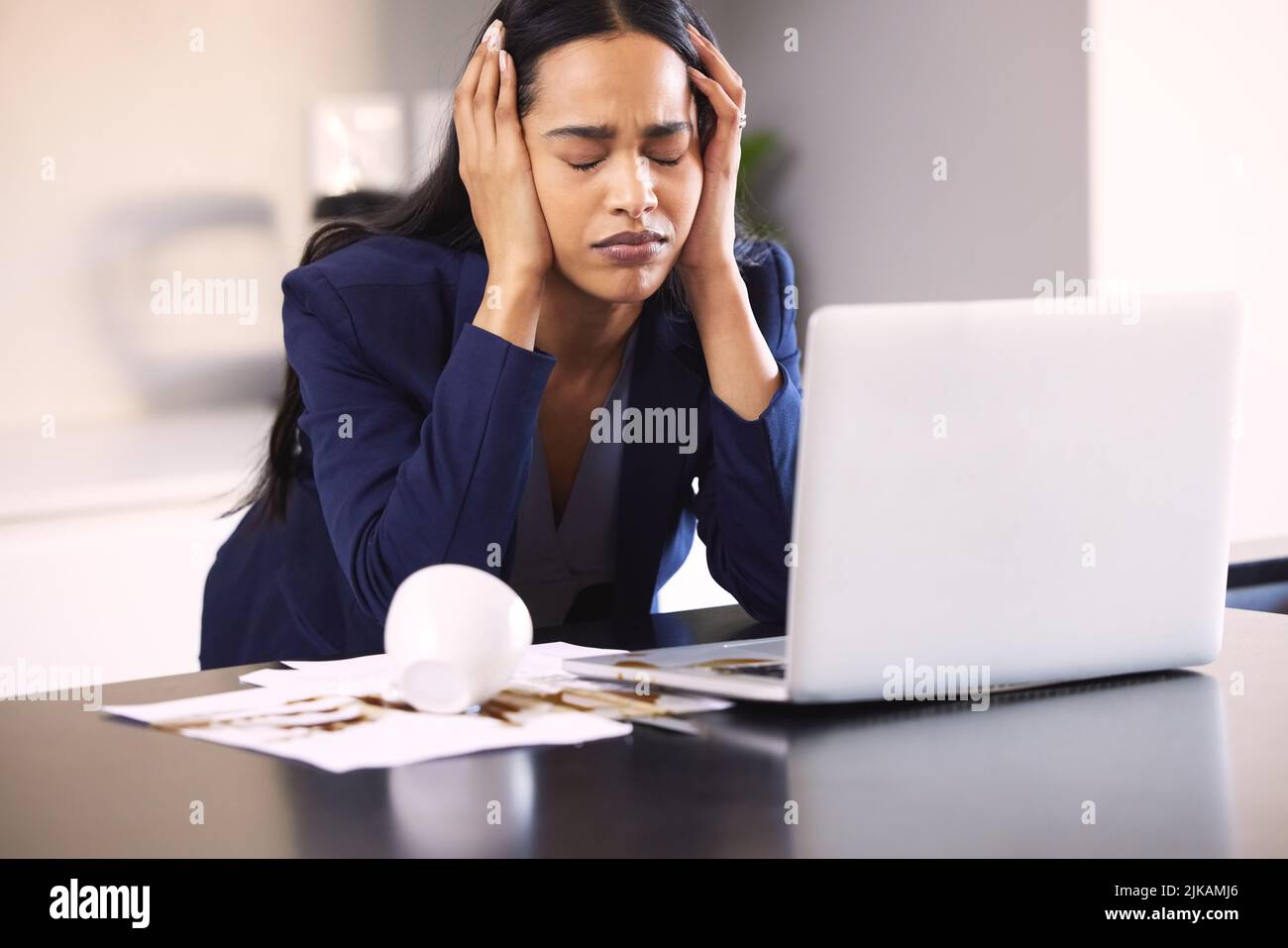 Può questo giorno peggiorare. Una giovane donna d'affari che cerca turbata per la fuoriuscita di caffè su un laptop e documenti su un tavolo. Foto Stock