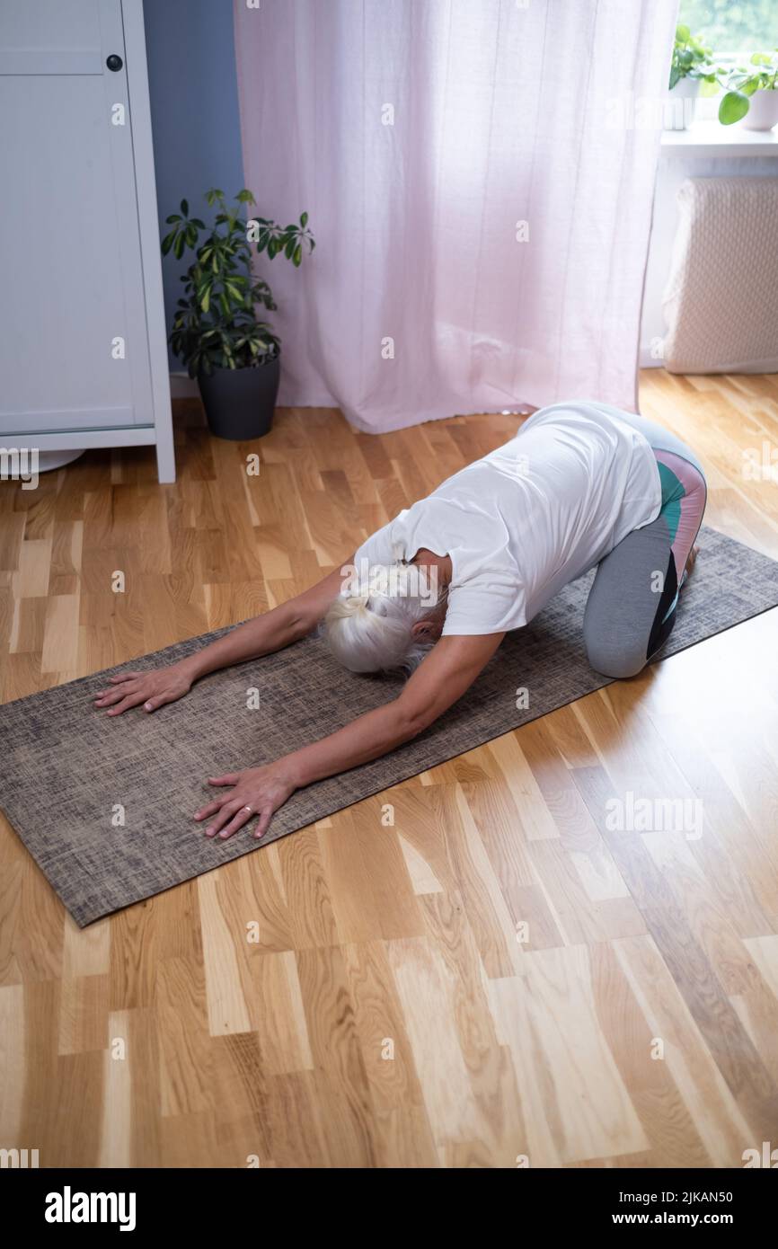 donna che si inginocchia su un tappetino e fa una balasana asana mentre pratica yoga a casa Foto Stock
