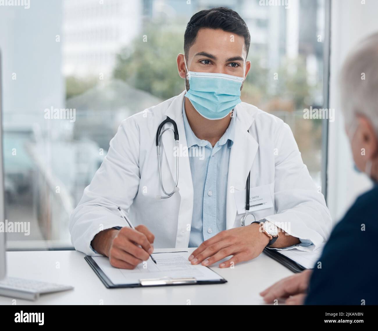 Può dirmi di più sui suoi sintomi: Un giovane medico che parla con un paziente in un ufficio. Foto Stock