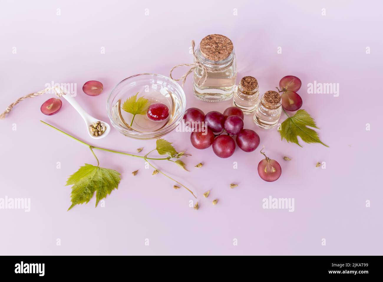 olio di semi di uva biologico in bottiglia di vetro con tappo di sughero, ciotola, con uva su sfondo rosa. cura della pelle facciale. produzione di colangen Foto Stock