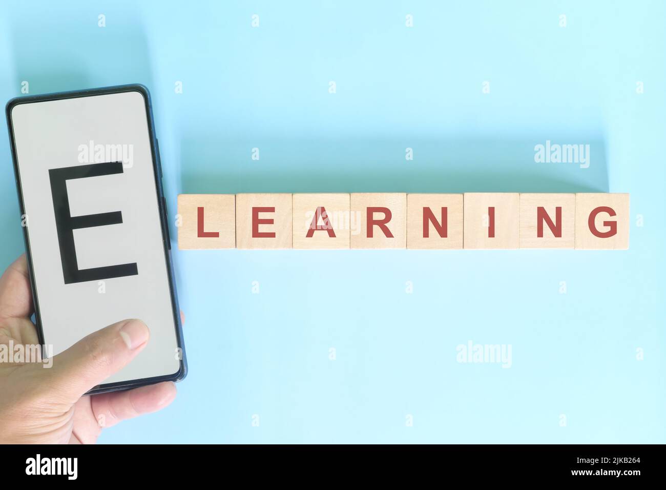 Apprendimento online o mobile o e-learning e concetto di istruzione. Telefono cellulare con supporto a mano accanto a blocchi di legno di testo tipografia. Foto Stock