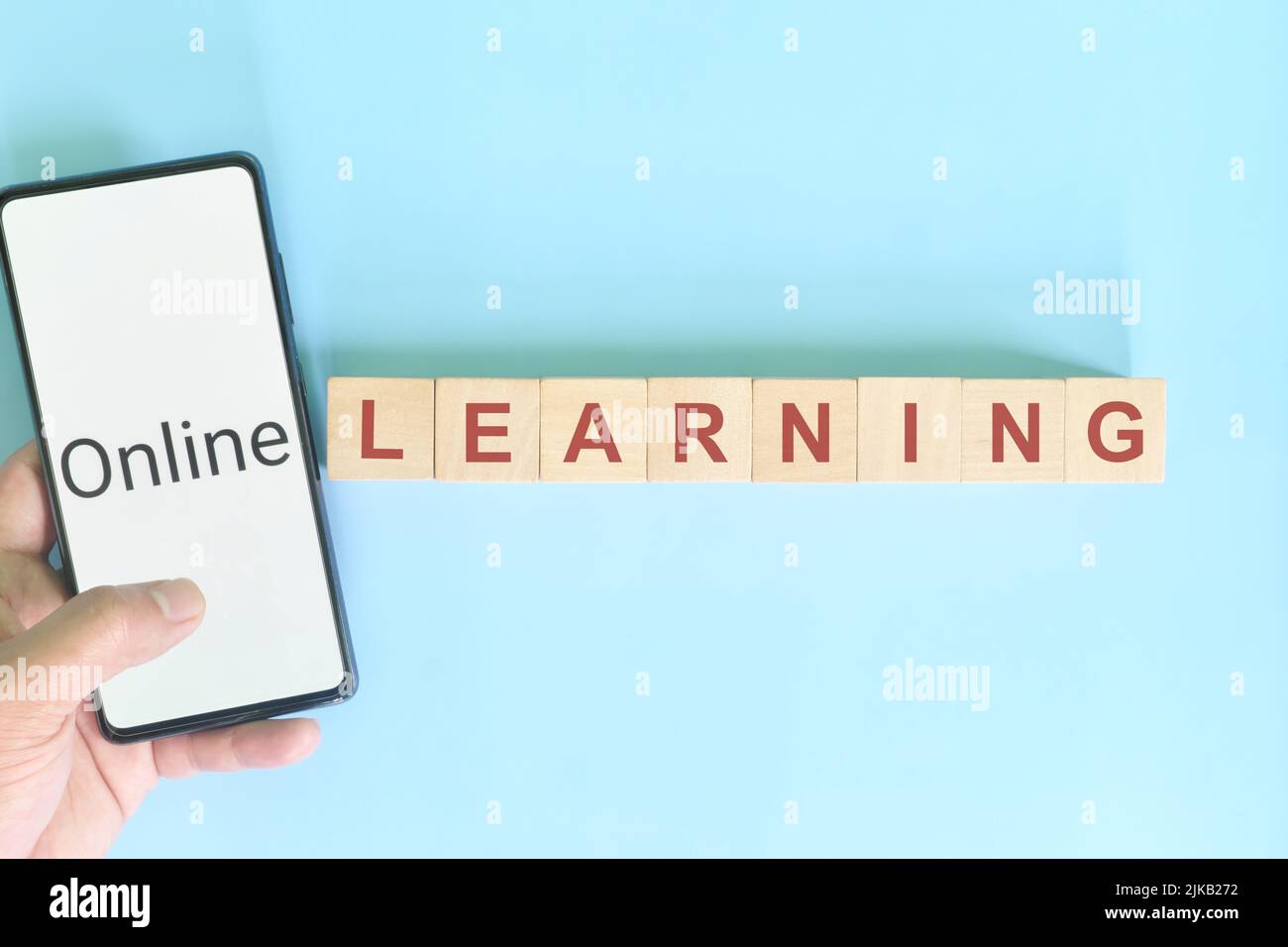 Apprendimento online o mobile o e-learning e concetto di istruzione. Telefono cellulare con supporto a mano accanto a blocchi di legno di testo tipografia. Foto Stock