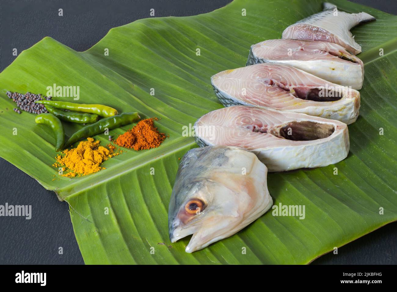 Pesce hilsa crudo tagliato a pezzi tenuto su foglia di banana per la cottura. Girato in studio con spazio copia sfondo e spezie. Foto Stock