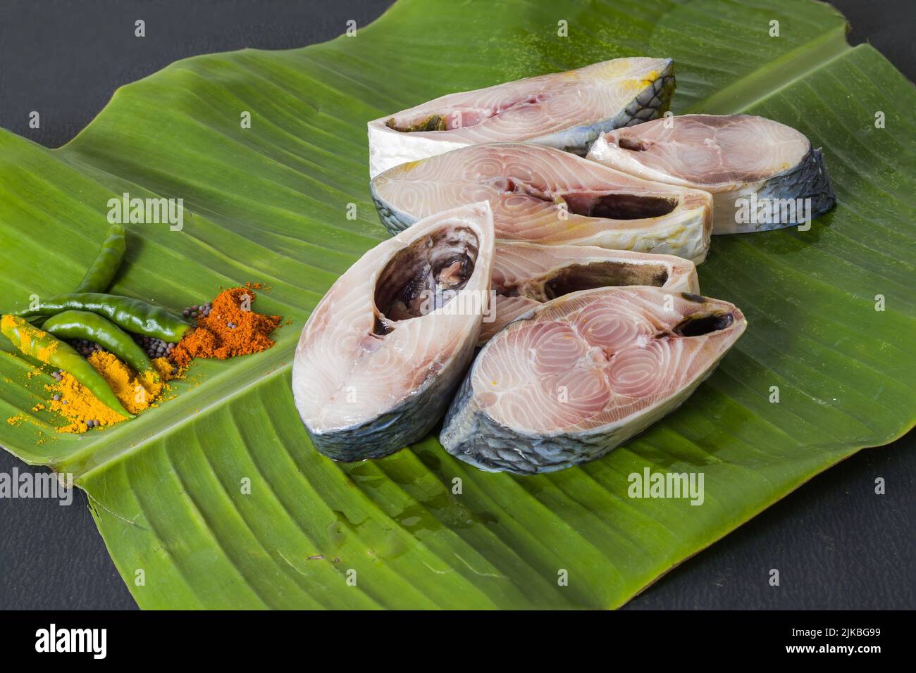 Pesce hilsa crudo tagliato a pezzi tenuto su foglia di banana per la cottura. Girato in studio con spazio copia sfondo e spezie. Foto Stock