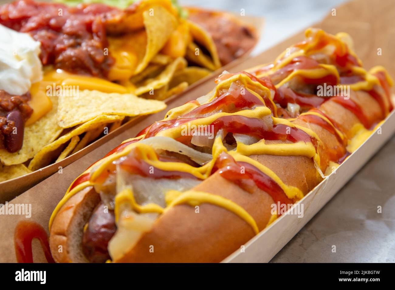 Cibo di strada hot dog soffocato in ketchup e senape con nachos chili serving suggerimento. Foto Stock