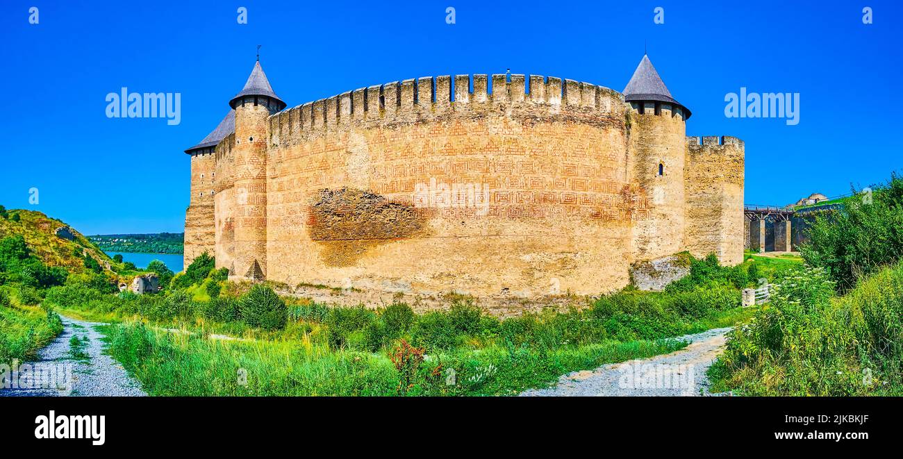 Godetevi la vista della spettacolare Fortezza medievale di Khotyn con lussureggiante vegetazione in primo piano e il Fiume Dniester sullo sfondo, l'Ucraina Foto Stock