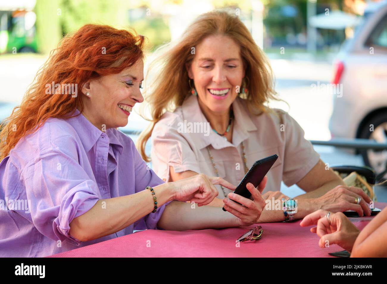 Donna matura che mostra lo smartphone alla sua amica a un tavolo in un ristorante. Foto Stock