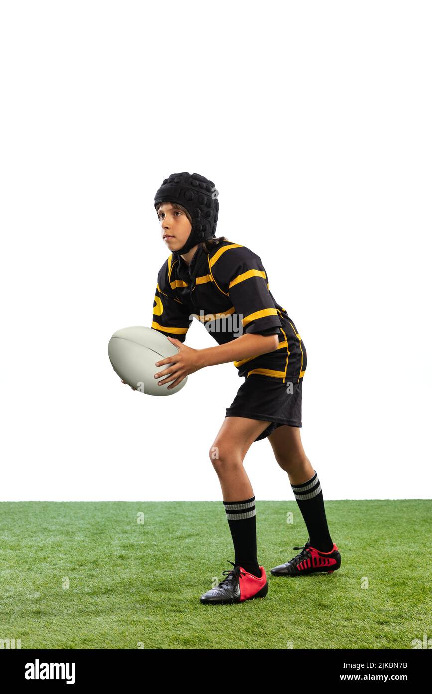 Ritratto di sportivo ragazzo, capretto, giocatore di rugby maschile allenamento con palla isolato su sfondo bianco con alluvione erba. Sport, squadra, studio, abilità Foto Stock