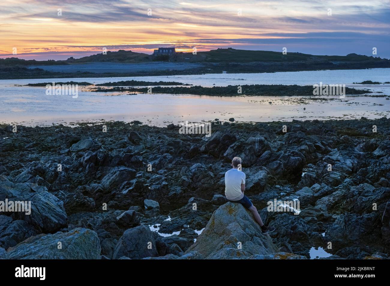 Un uomo che guarda il sole tramontare sull'isola di Lihou da l'Erée, Guernsey, Isole del canale Foto Stock