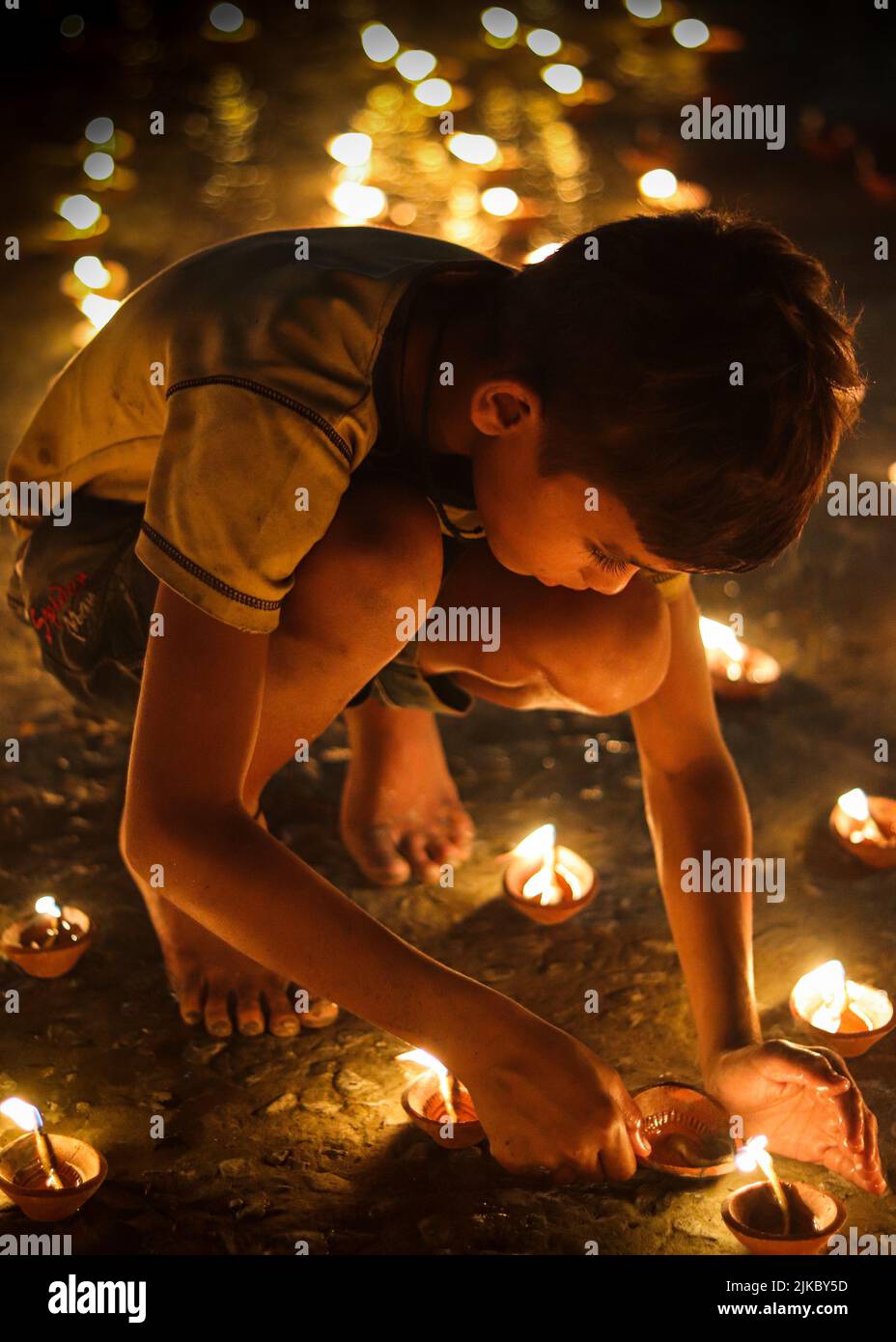 Un ragazzo che illumina la sua candela a terra all'aperto a tarda notte Foto Stock