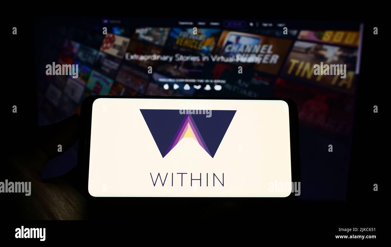 Persona che tiene uno smartphone con il logo della società di realtà virtuale all'interno di Unlimited Inc. Sullo schermo di fronte al sito Web. Mettere a fuoco sul display del telefono. Foto Stock