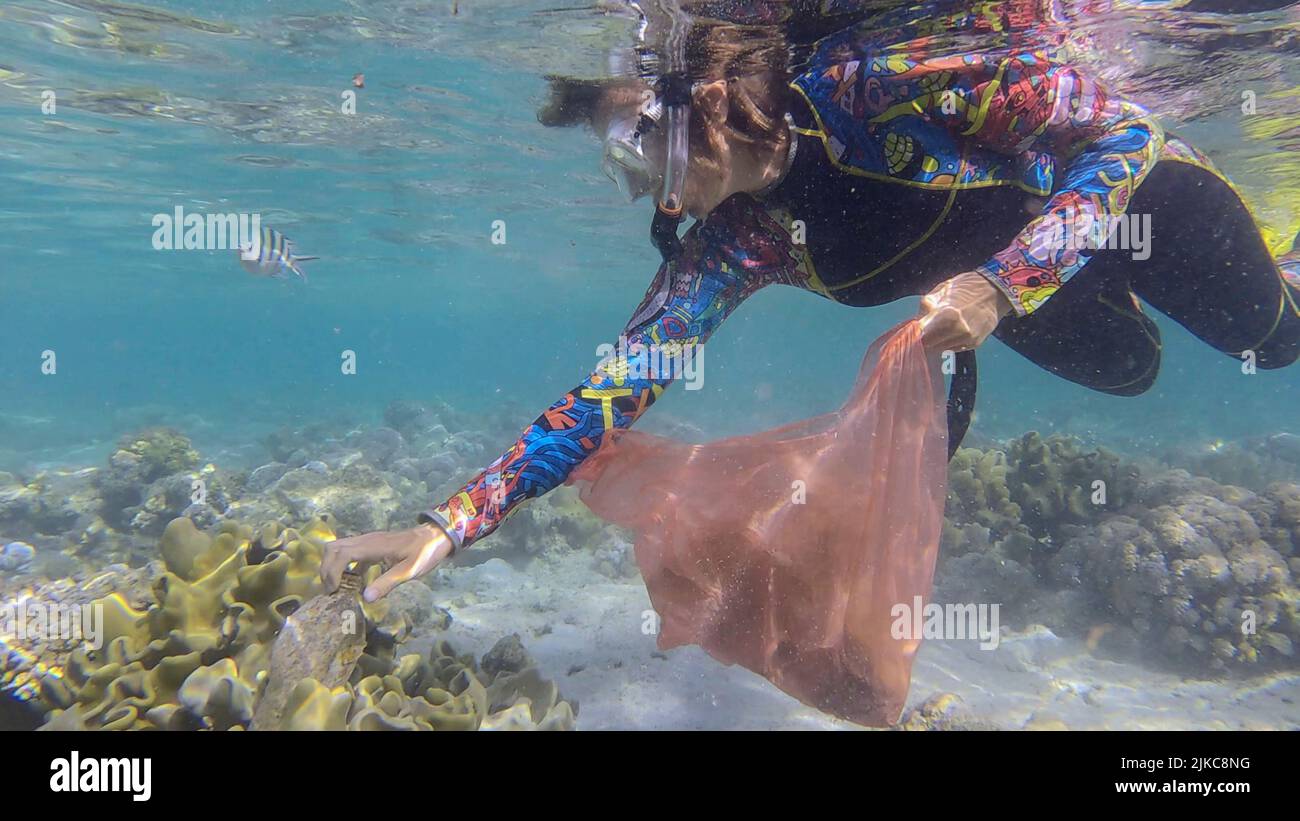 La donna in attrezzatura subacquea nuota e raccoglie i detriti di plastica sott'acqua sul fondo della barriera corallina. Lo snorkeler pulisce l'Oceano dall'inquinamento di plastica. P Foto Stock