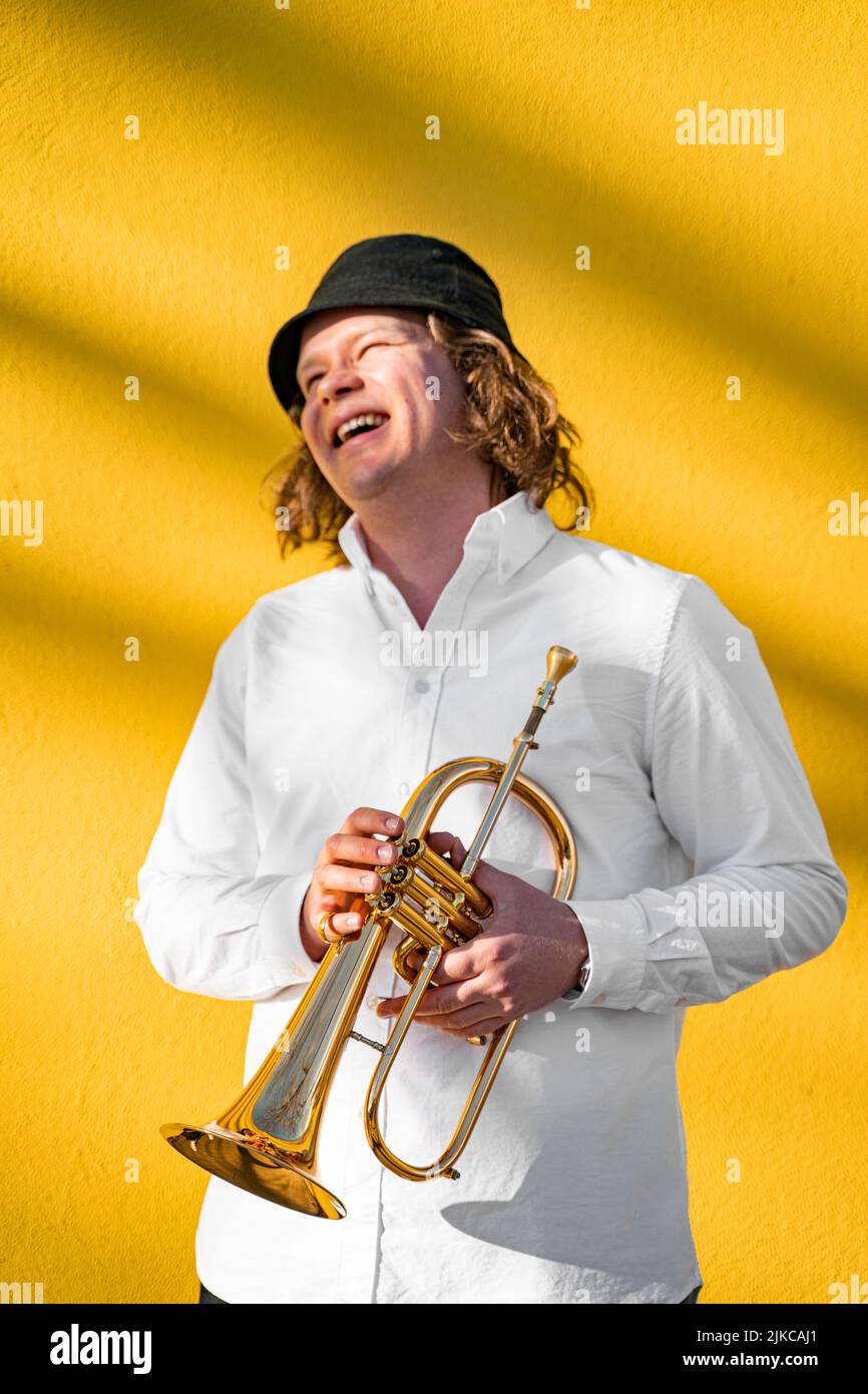 Giovane caucasico a capelli lunghi biondo allegro uomo sorridente con tromba all'aperto Foto Stock