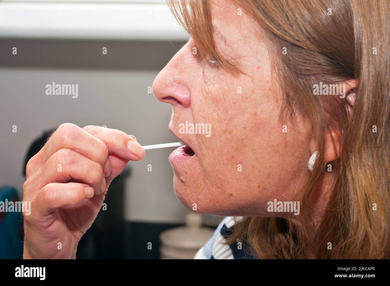 Donna Femminile nel suo 60s facendo un test Covid LFT nella sua gola della bocca Foto Stock