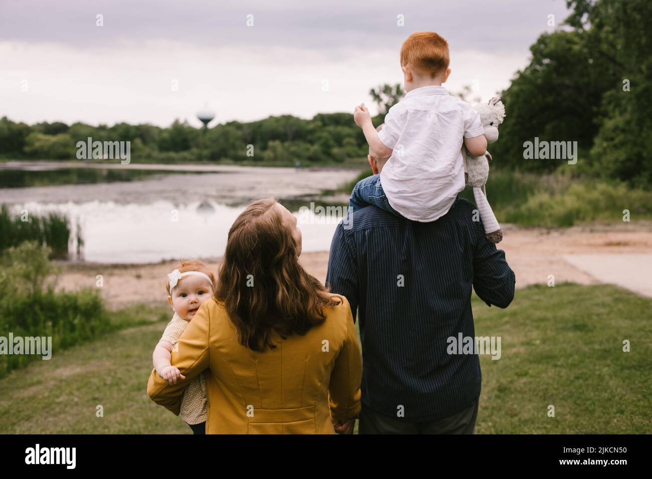 Famiglia di quattro persone con capelli rossi passeggiate sul lago con alberi verdi Foto Stock