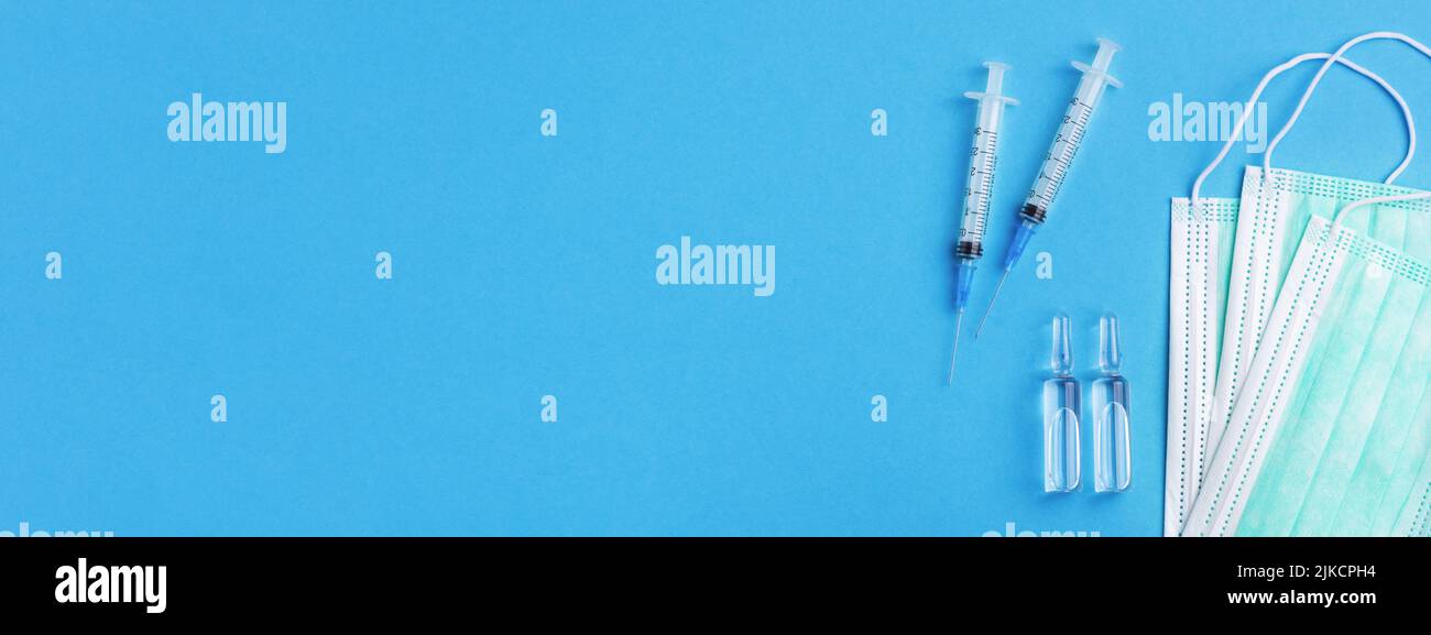 Maschere mediche, iniezione affilata ago e farmaci in flaconcino su sfondo blu chiaro. Banner per sito web con spazio per la copia. Foto Stock