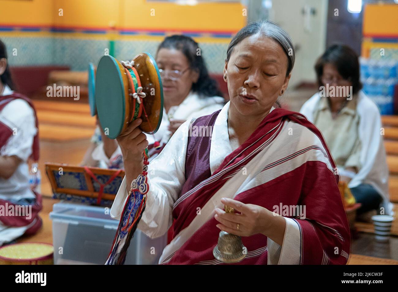 Un devoto buddista Nepalese donna orante in un tempio mentre il terminale voce squilla una campana e la rotazione di un tamburo damaru. In Elmhurst, Queens, a New York City. Foto Stock