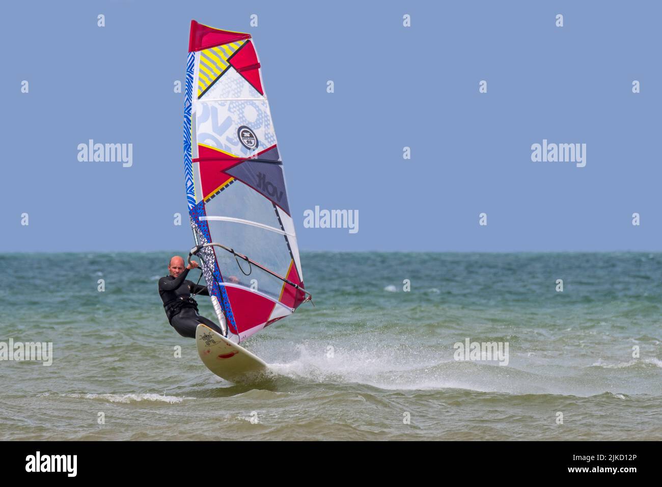 Windsurf ricreativo in muta nera che pratica il windsurf classico lungo la costa del Mare del Nord Foto Stock
