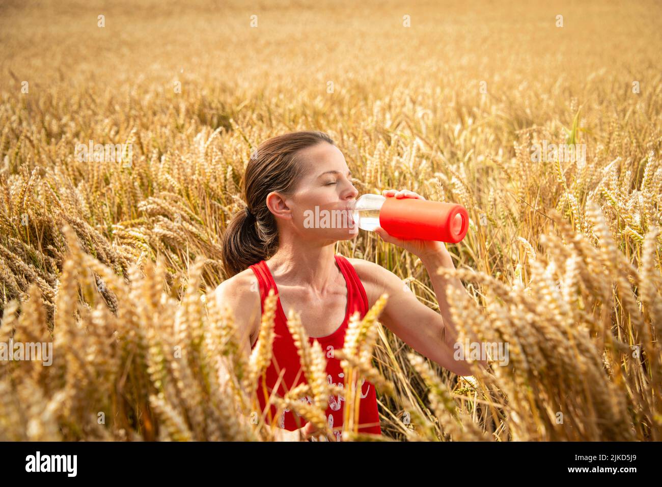 Donna che beve acqua da una bottiglia in un'onda di calore, campagna. Foto Stock